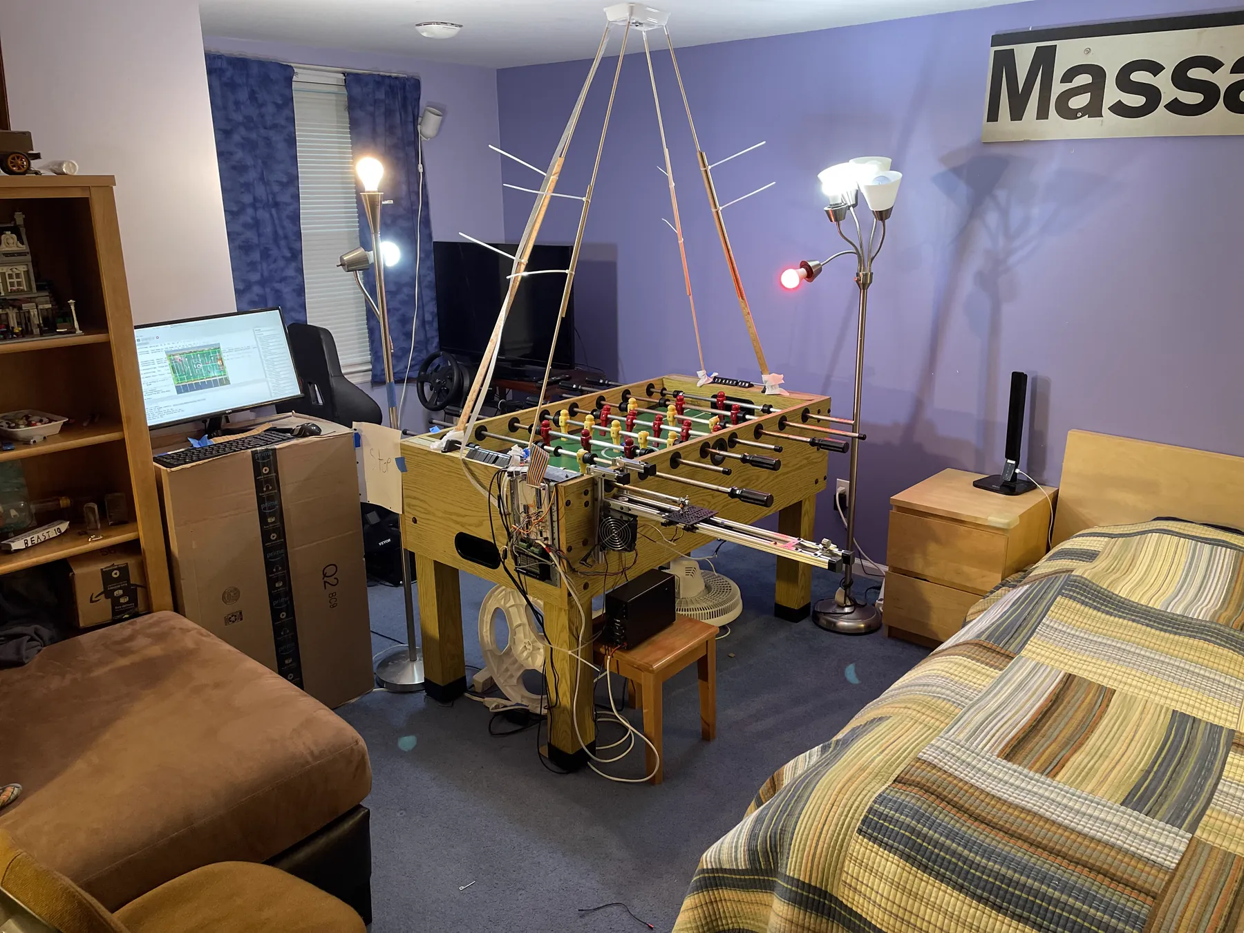 Wide view of the finished build: the foosball table with the dowel camera rig suspended overhead, KURT's rail and electronics on the near side, and the tracker running on the monitor at the left