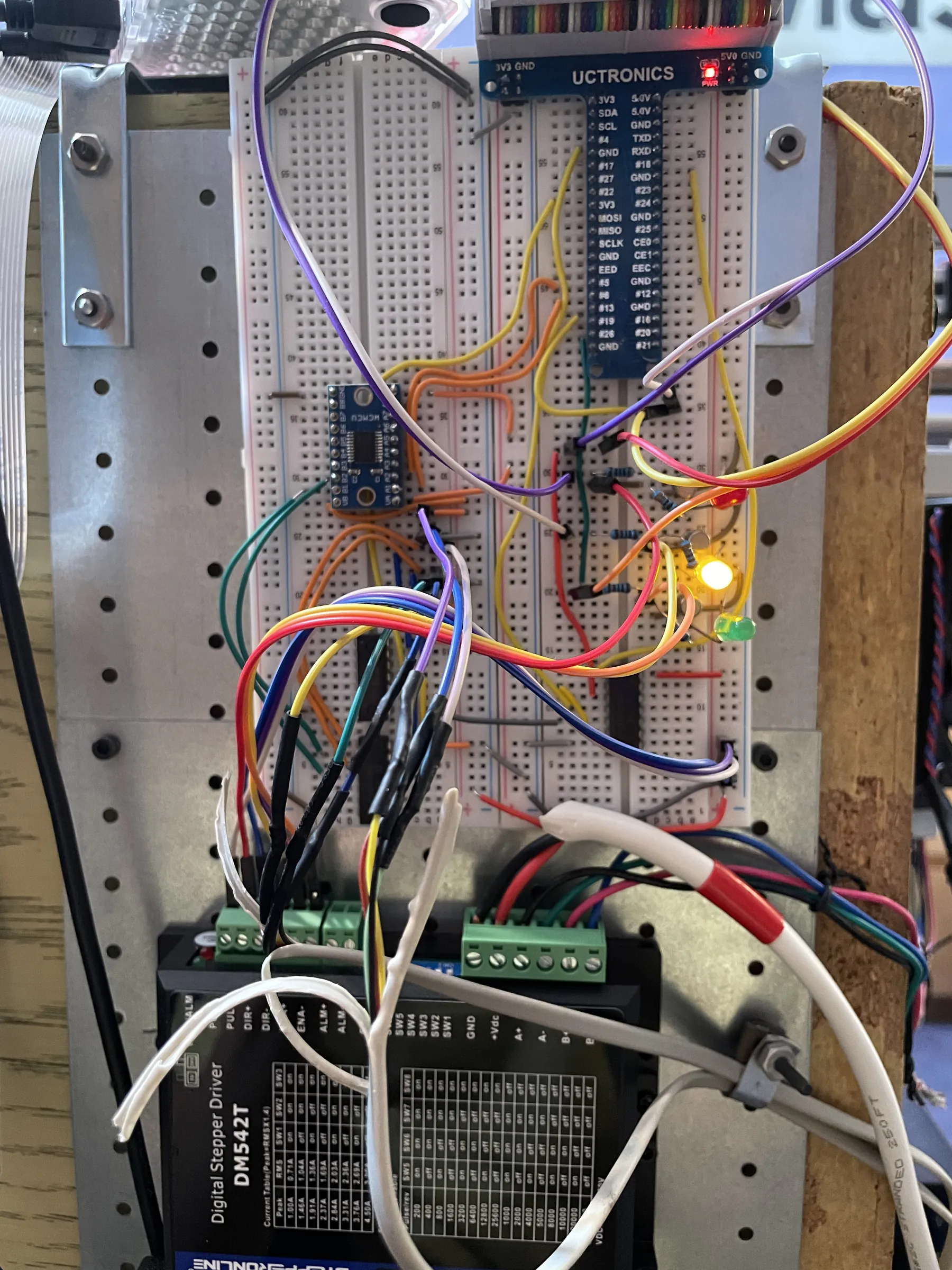 The wiring panel: a breadboard fed by the Raspberry Pi GPIO breakout ribbon, mounted above a DM542T digital stepper driver